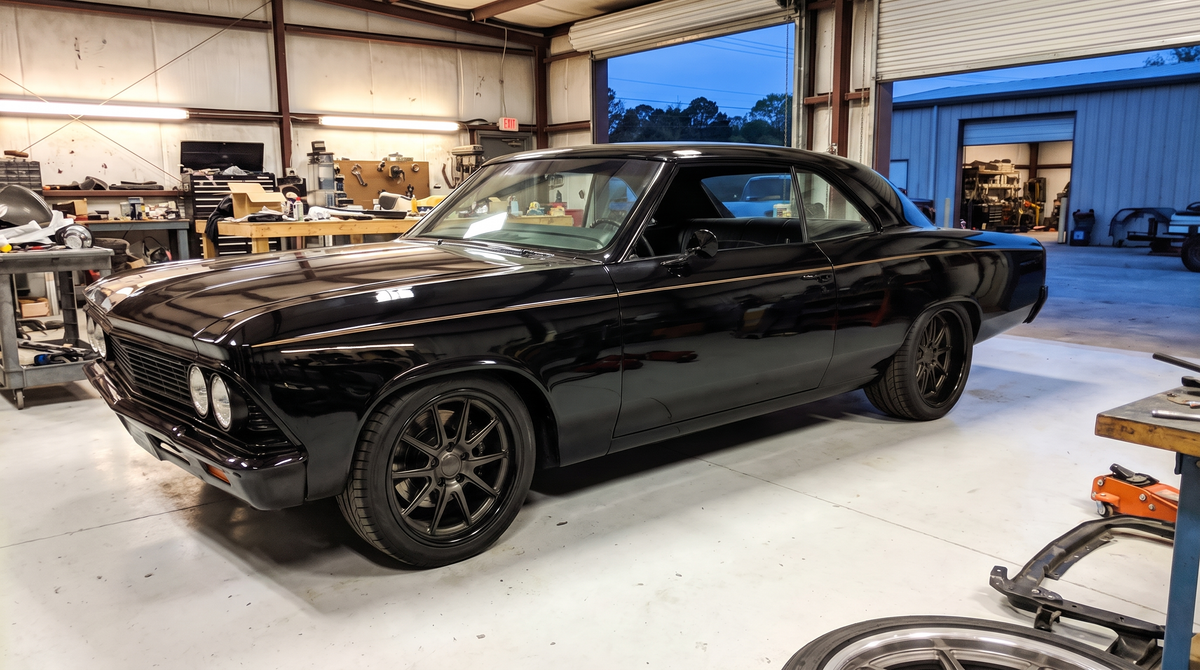 Black pro touring 1966 Chevelle with flush mount glass parked in a restoration shop at dusk