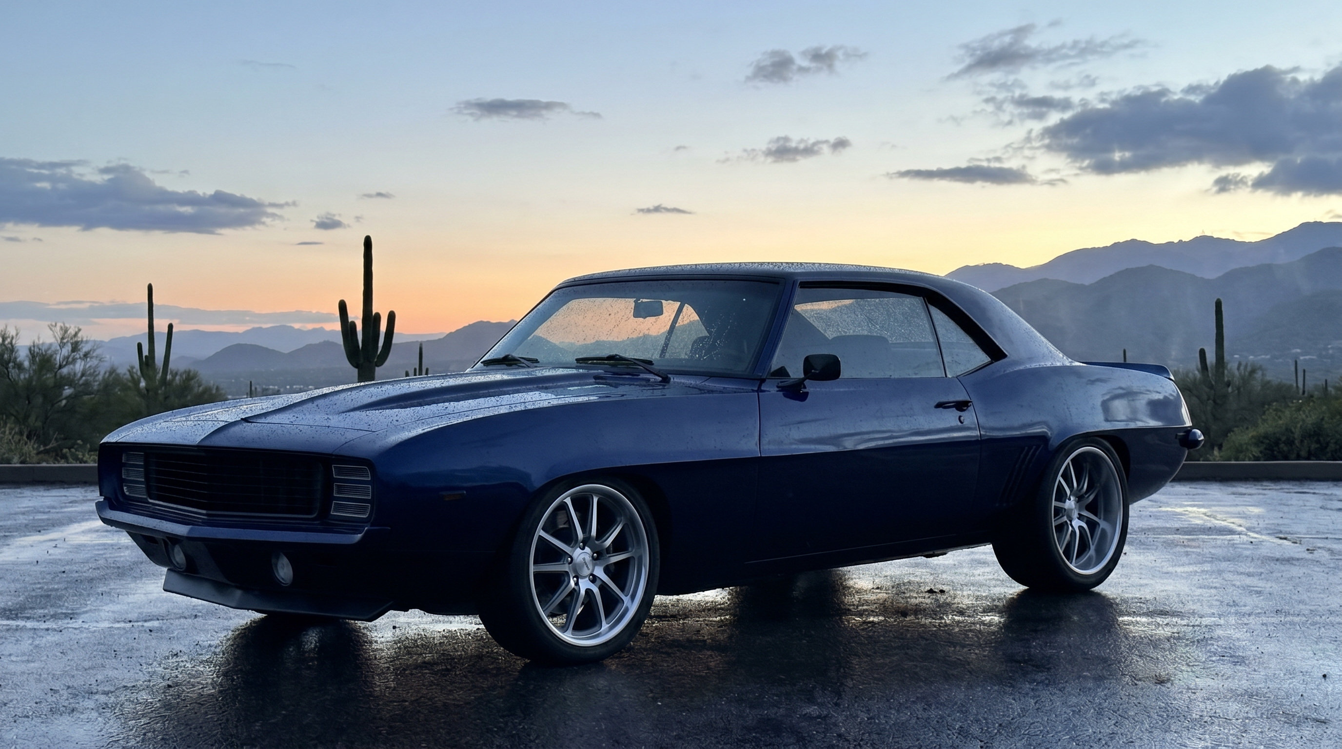 Pro-touring 1969 Camaro with flush-mount glass beaded with rain at a Phoenix desert overlook at blue hour
