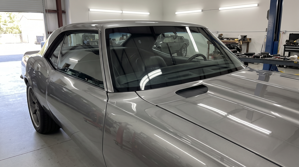 Silver pro-touring muscle car in a shop shot through the flush-mount windshield showing the dash and cowl area