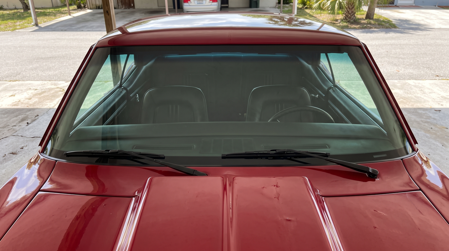 Head-on view of a classic muscle car windshield in shade showing the green tint of laminated glass and a trimless flush-mount edge